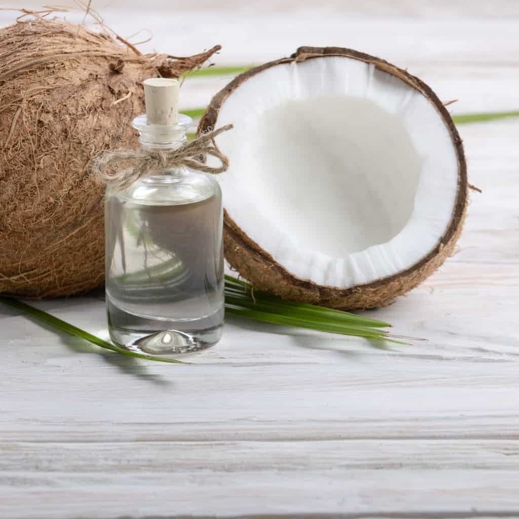 Coconut oil in glass jar and shell pieces on white wooden table